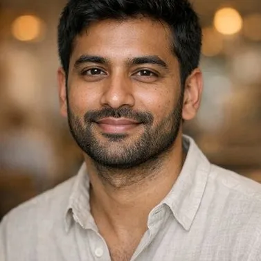 Young South Asian man, trimmed beard, thick dark hair, relaxed open-collar shirt